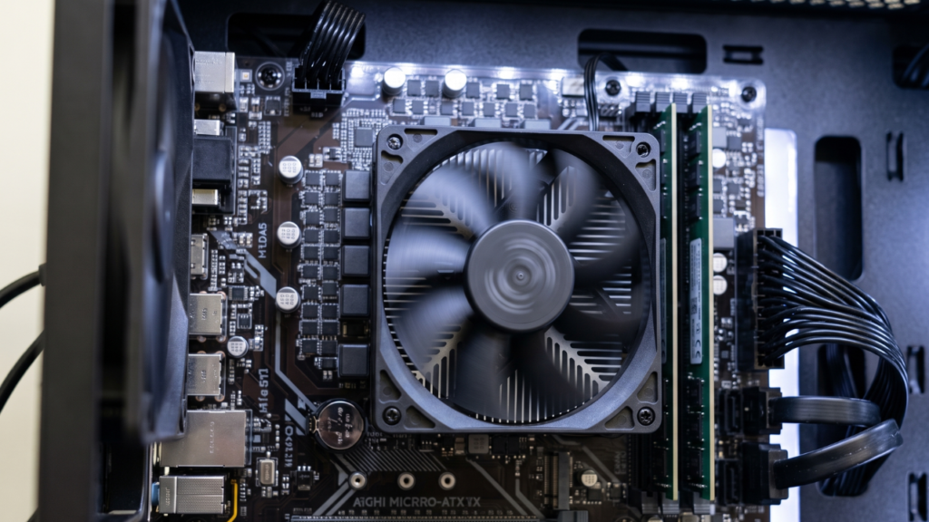 An Intel Core i5-12400F processor installed on a budget motherboard inside a running PC, showing the stock cooler spinning.